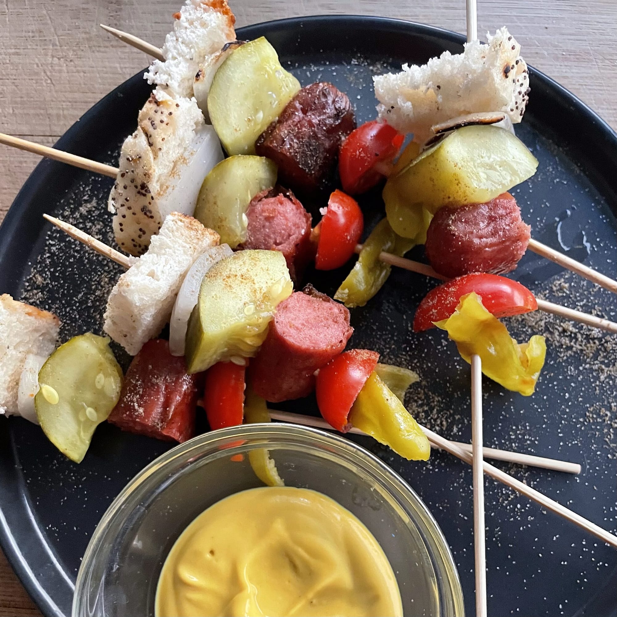 pieces of chicago style hot dog on a skewer laid on a plate with mustard serving dish