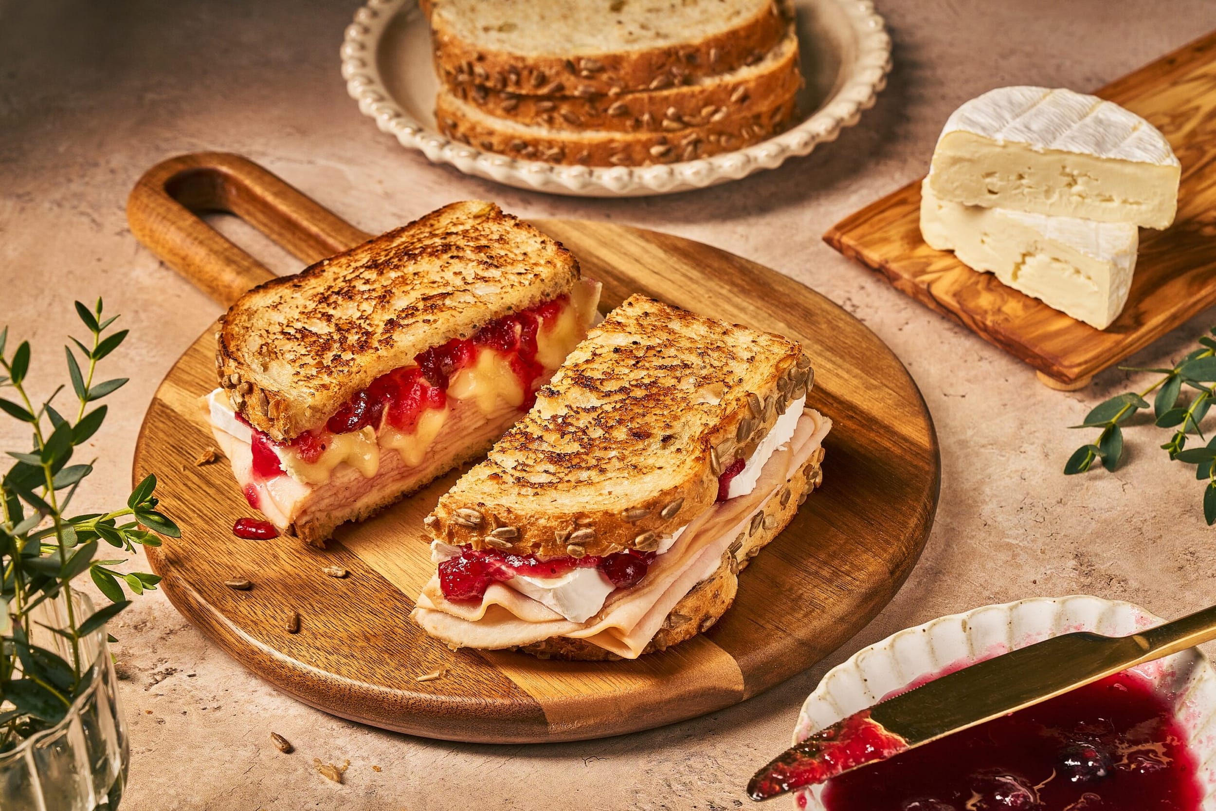 Seeded sourdough bread sandwich with brie, jam, and turkey placed on wooden cutting board on a counter