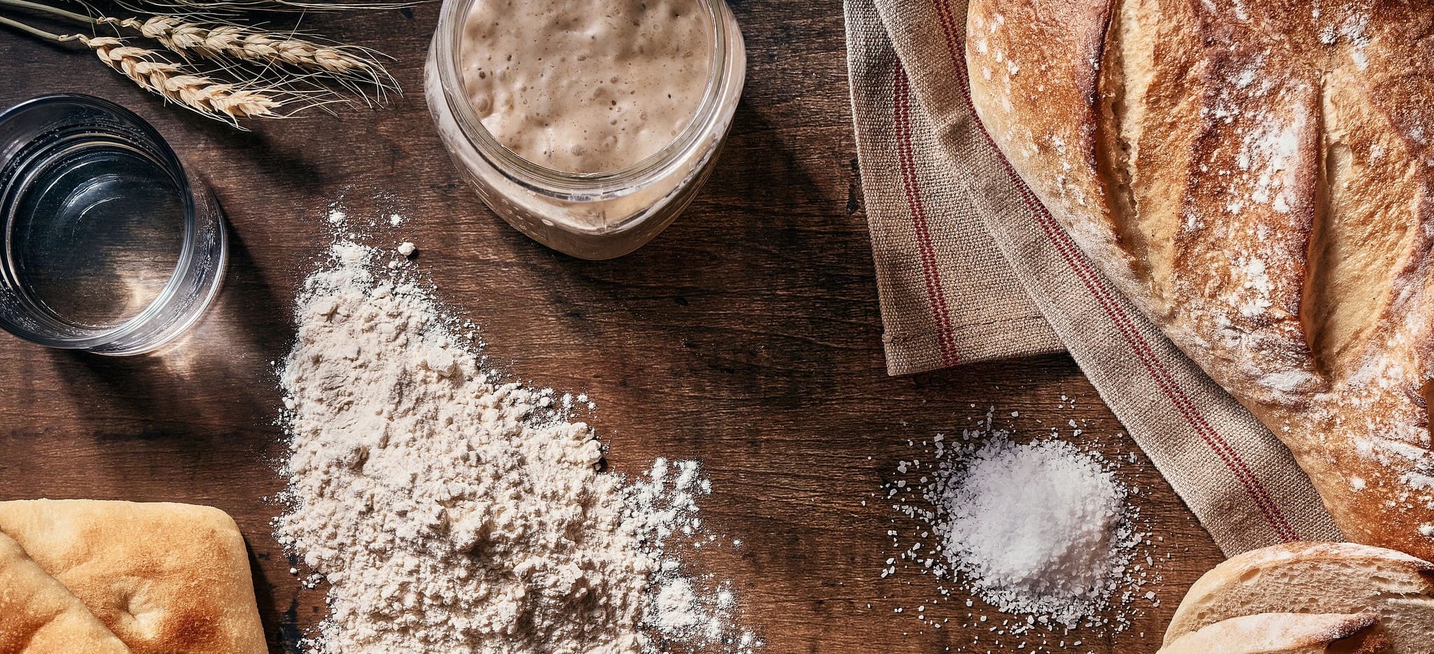 sourdough bread, flour, water, sat, and wheat leaves on dark wood table
